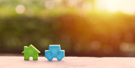 Blue car models and Green house models are located on wooden boards with a natural garden...