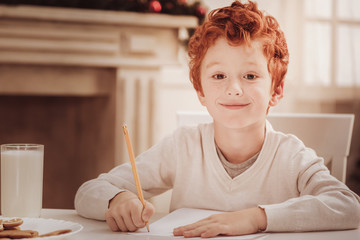 Spending time with pleasure. Close up of diligent little boy looking at you while sitting at the table and drawing