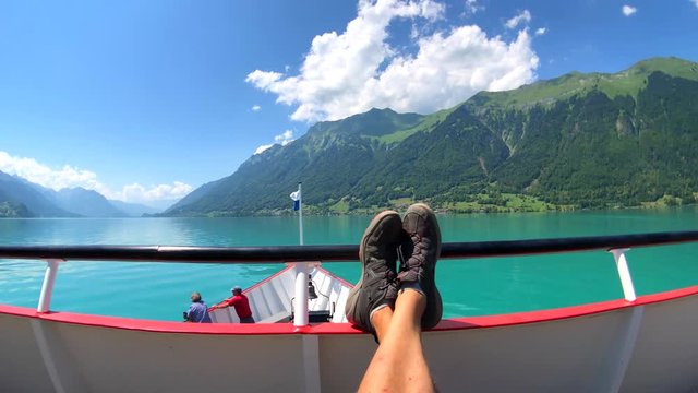 POV travelling by boat at Brienz lake at summer time in Switzerland. Tourists feet at foreground