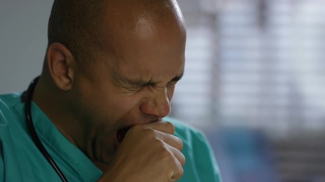 Tired male nurse working on laptop in hospital office