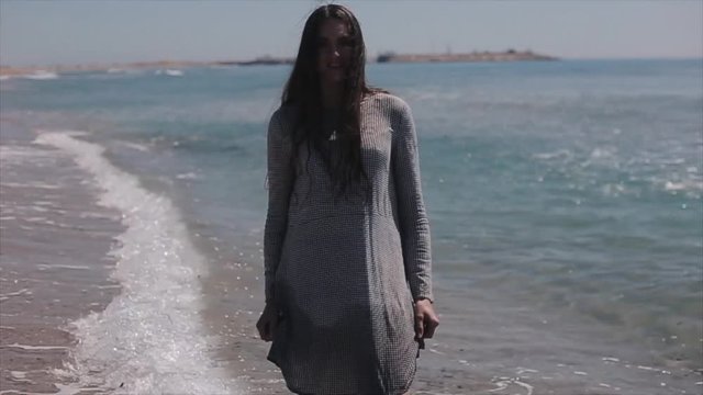 A beautiful girl in a dress walking backwards along the beach. Slow motion