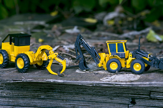 There are two  excavator toy cars on wooden boards stacked in the open woods.