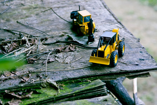 A scene from the top of two bulldozer toy cars on wooden planks in an outdoor forest.