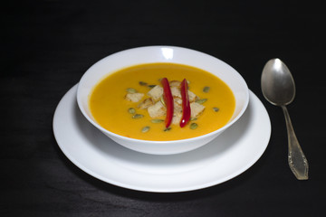 pumpkin soup with paprika, seeds, garlic, rusks and greens on dark background