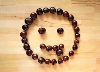 Smiley aus Kastanien Maronen braun, glänzend auf Untergrund aus Holz. Lächelt  Zunge raus,...