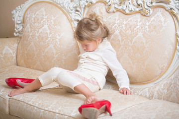 Kid with unhappy face sit on sofa with red shoes