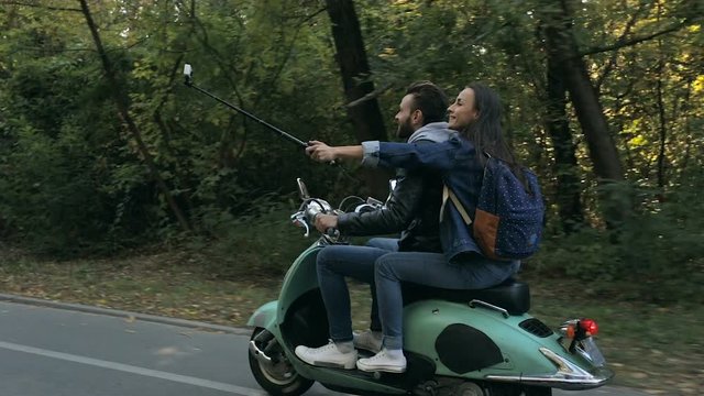Happy couple in the trip. Riding on their scooter. Woman shooting video on the action camera, using selfiestick.