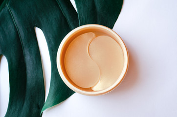  Monstera leaf on white with a bottle of gold patches for the eyes. Eyelid skin care concept