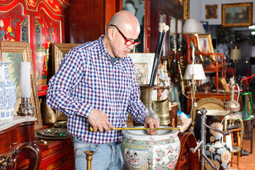 Experienced appraiser of antiques shop measuring antique vase while determining value