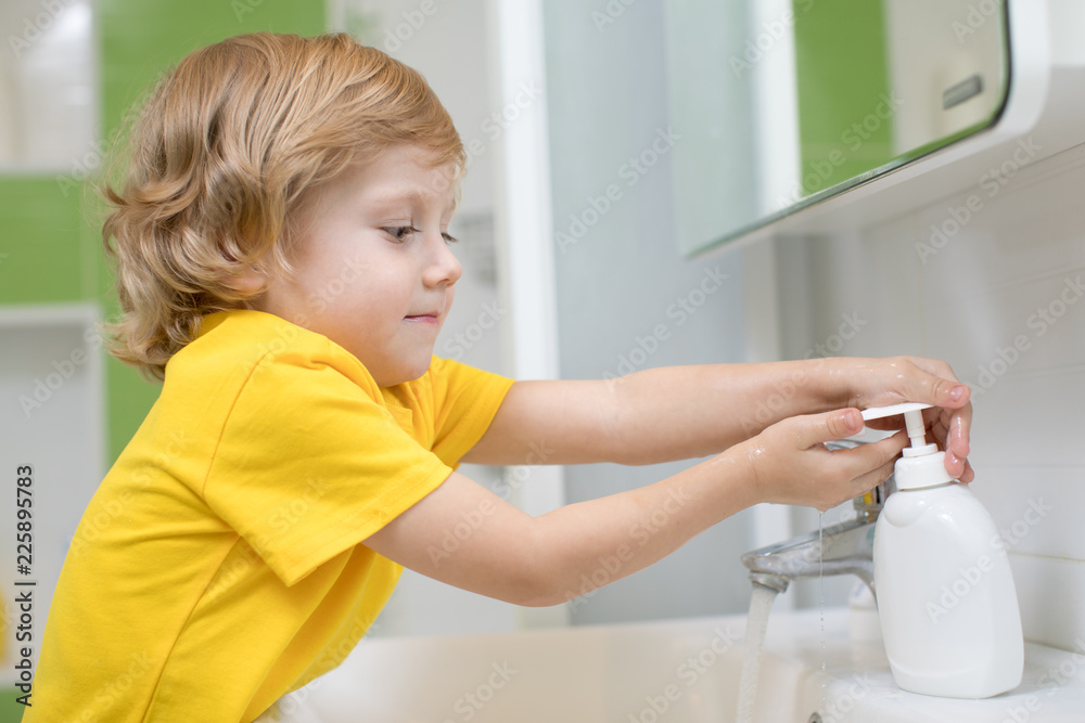 Wall mural Cute kid boy washing his hands in bathroom