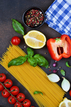 Italian food background. Ingredients for cooking pasta: spaghetti, tomato, basil and pepper on a dark concrete background.