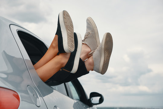 Two Pair Of Legs Wearing Sneakers Out The Car Window