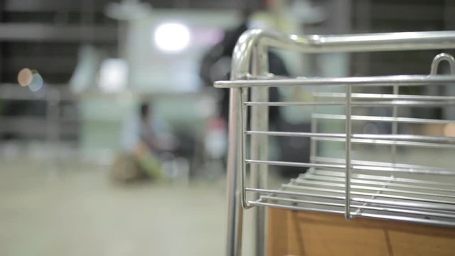 airport luggage cart standing in departure or arrival zone with blurred people at the background waiting for their gate opening. Metal and plastic Hand held shot. Time waste concept