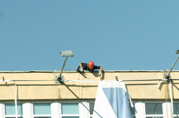 An industrial climber hangs an advertising banner on a commercial building extreme, against the blue sky