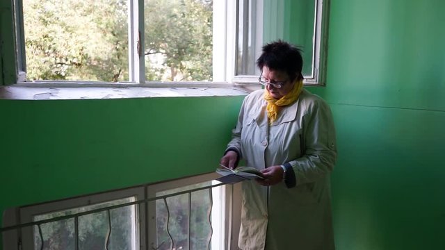 elderly woman reading a book near the window MLS