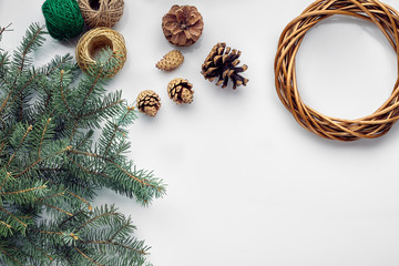 Beautiful festive handmade wreath base with three bumps near it, threads and twigs blue Christmas tree on the white table background, flat lay. © nazarovsergey