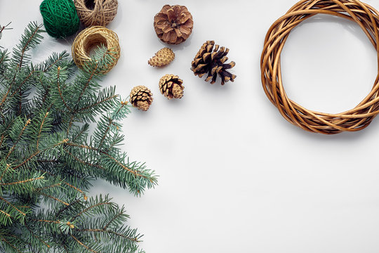 Beautiful festive handmade wreath base with three bumps near it, threads and twigs blue Christmas tree on the white table background, flat lay.