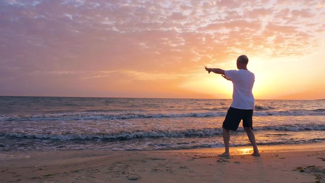 Man training Tai Chi chuan while morning sunrise in sky at sea beach