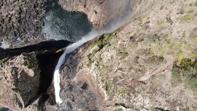 Aerial drone shot 120m above wallaman falls. Shot moves over the edge of the waterfall and continues past to a 200m drop, overlooking a lake and valley.