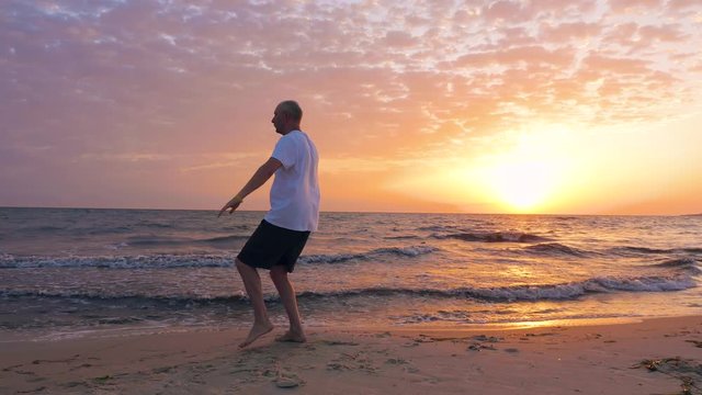 Man training Tai Chi chuan while golden sunset at evening sea shore