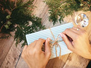 Christmas gift in hands, pine cones, thuja branches on wooden background. Flat lay, top view, copy...