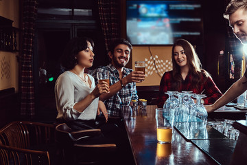 Group of happy multiracial friends resting and talking at bar or pub.