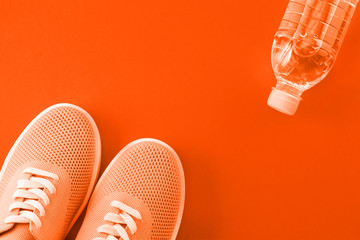 Light orange sneakers and a bottle of water on a orange background.