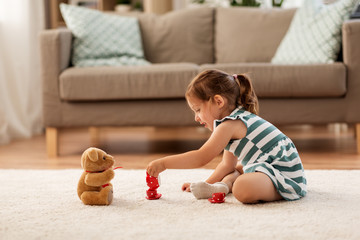 childhood and people concept - happy three years old baby girl playing tea party with toy crockery and teddy bear at home