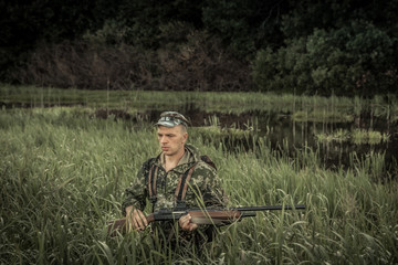 Hunting hunter brutal man breaking through swamp tall grass during hunting season