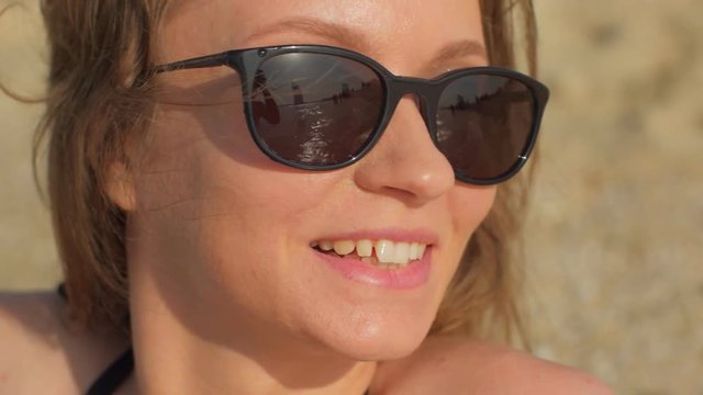 smiling pretty woman with black sunglasses on a beach in sunny summer day, closeup