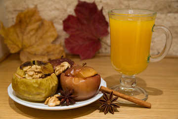 Tea with sea-buckthorn and spices. Baked apples, red and yellow, stuffed with raisins and nuts (walnuts and almonds), cinnamon and anise spices. Autumn dried leaves and brick walls background.