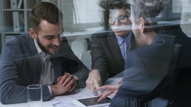 Tilt up shot of three businesspeople using tablet computer when discussing apartment blueprints