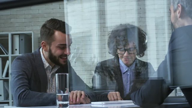 Zoom in shot of smiling businesspeople studying blueprints and using tablet computer in office with glass walls