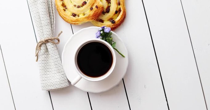 Delicious pastry rolls of snails with raisins and a cup of black coffee. Top view. Composition on white wooden table.
