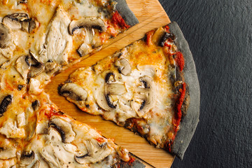 Pizza with champignons and chicken breast on black dough.