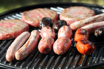 Shallow focus shot of tasty assorted delicious sausages and burgers sizzling and cooking on a barbecue griddle plate, outside in bright summer sunshine