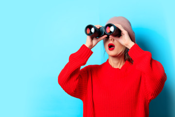 Portrait of a young girl in red sweater with binocular on blue background