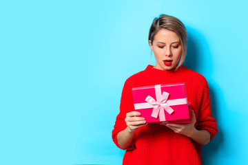Fototapeta premium Portrait of a young girl in red sweater with gift box on blue background