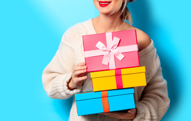 Portrait of a young girl in white sweater with gift colored boxes on blue background
