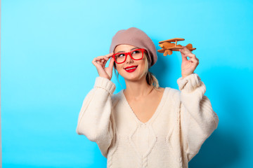 Portrait of a young girl in white sweater with wooden toy plane on blue background