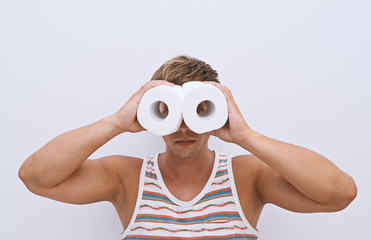 Handsome guy looks through rolls of toilet paper and simulating binoculars. Finding solutions to...