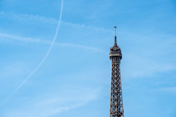 Fototapeta na wymiar Eiffel tower detail against blue sky with plane traces on clear sky - sign of Paris and symbol of France