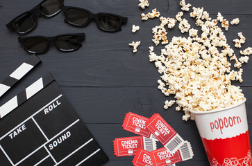 Movie time, flat lay with space for text. Cinema minimal concept. Movie clapperboard, 3d glasses, movie tickets and popcorn on a black wooden background.