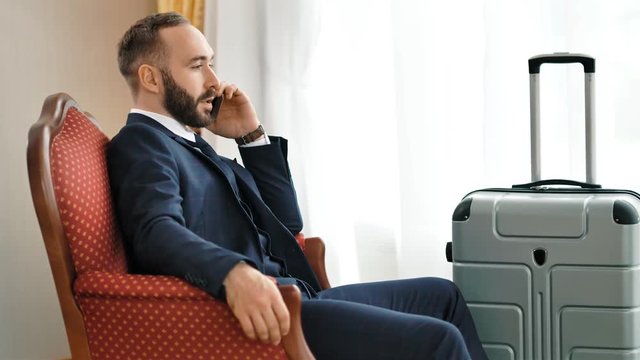 Confident stylish male businessman discussing problem talking using smartphone at hotel room