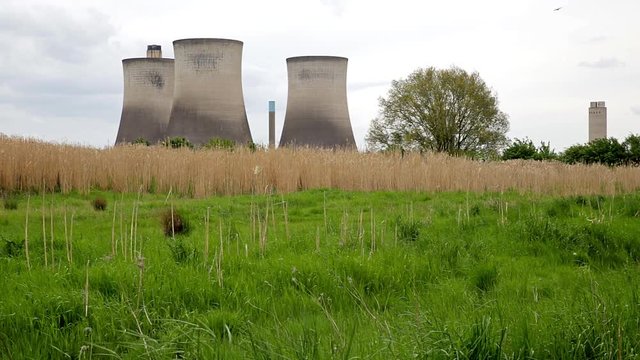 Power station cooling towers and chimneys beyond water meadow with trees