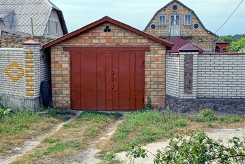Fototapeta na wymiar brick garage with red iron gates and part of the fence in green grass