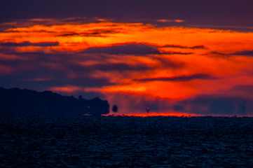 Fototapeta na wymiar 岬の沖で朝焼けに染まる雲と灯浮標のあかり