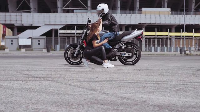 Beautiful Ukrainian woman sitting with gun in hand on bike races. Attractive Caucasian guy riding motorcycle, five-giving to girl. Outdoors.