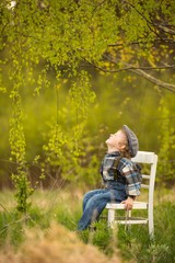 Young blonde boy relaxing on white old chair in spring landscape