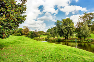 Fototapeta na wymiar Green lawn and trees at river under blue cloudy sky.